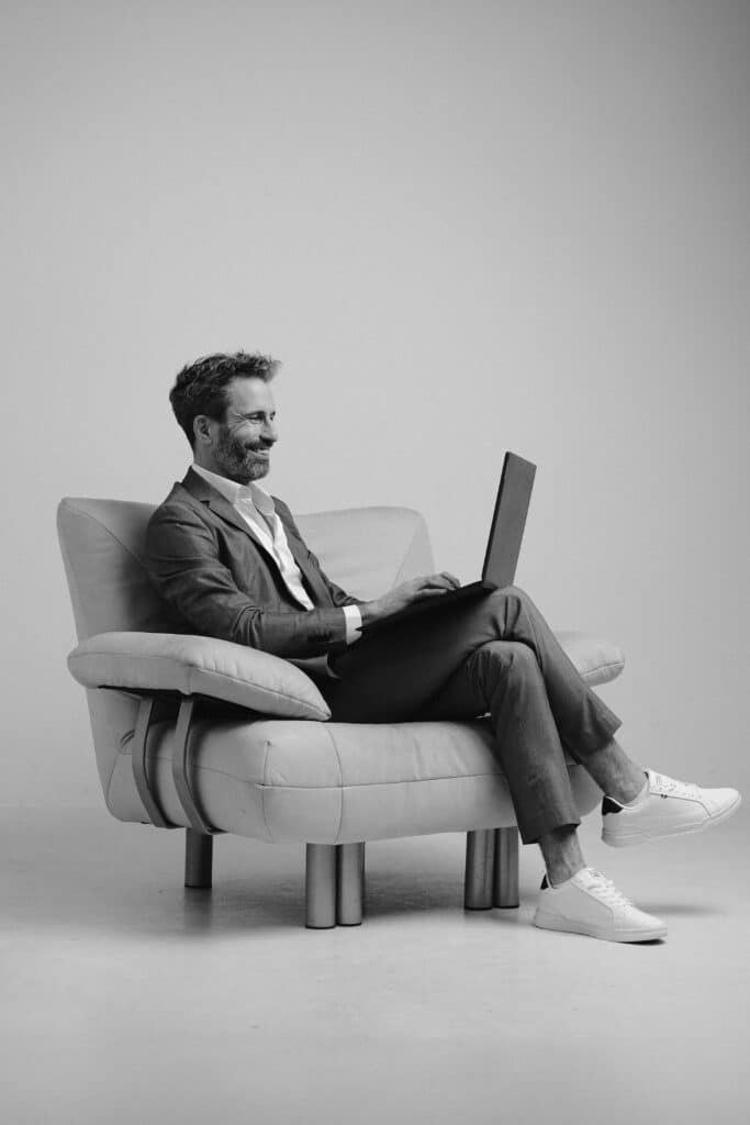 Business Mann im Anzug arbeitet mit Laptop in modernem Sessel – Schwarzweiß Portrait