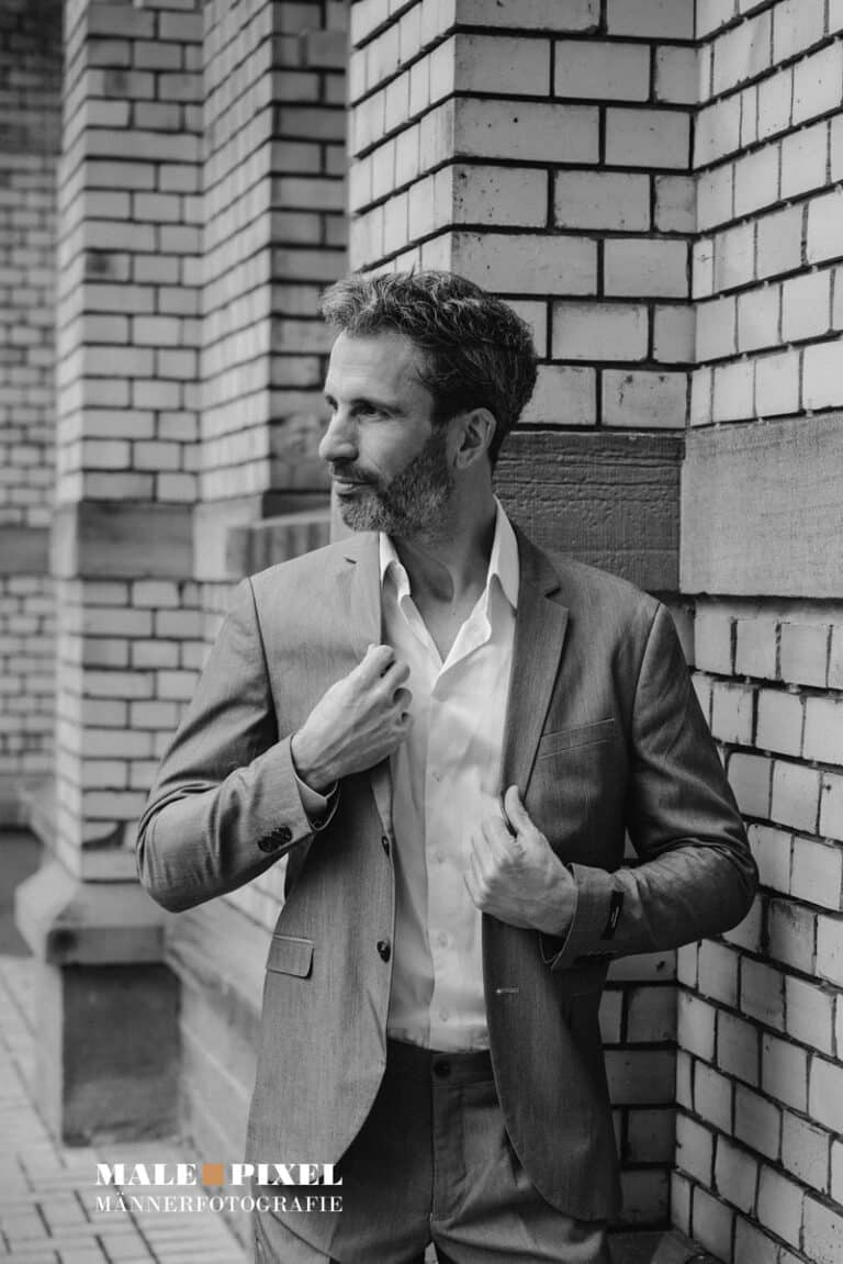 Eleganter Mann im Anzug vor Backsteinfassade – Schwarzweiß Editorial Portrait