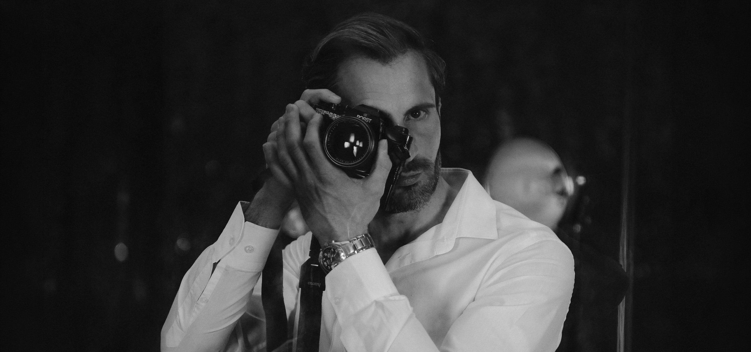 Mann mit Kamera vor dem Gesicht im Schwarzweiß-Charakterportrait
