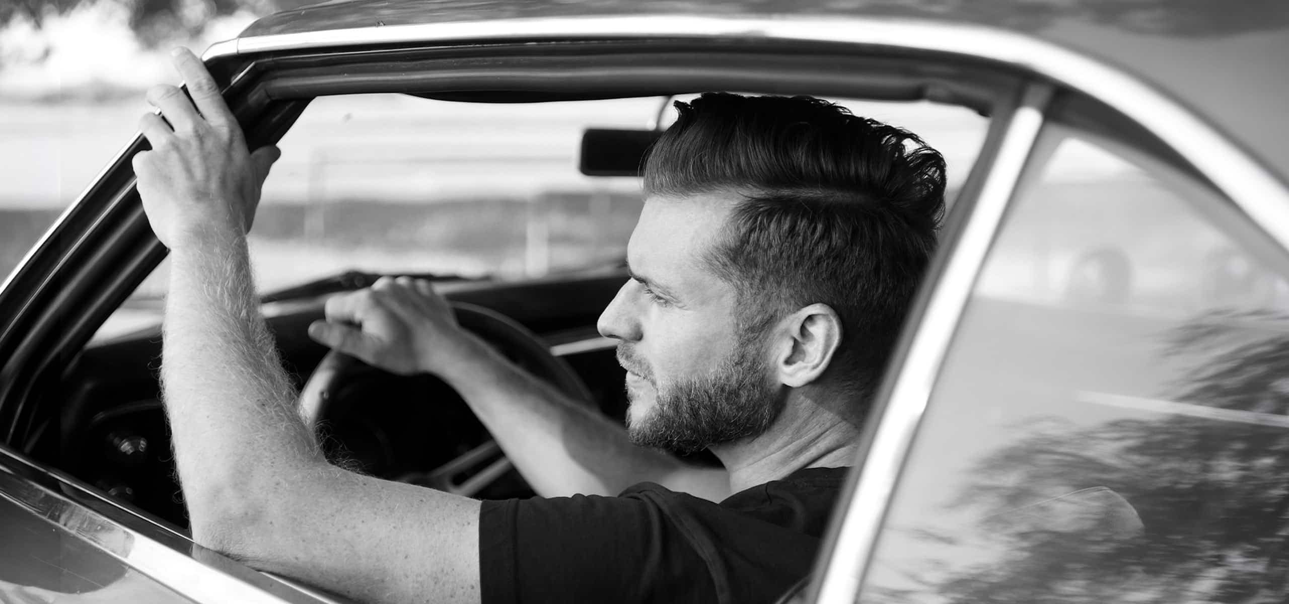Mann sitzt am Steuer eines klassischen Autos – Schwarzweiß Männerportrait im Oldtimer